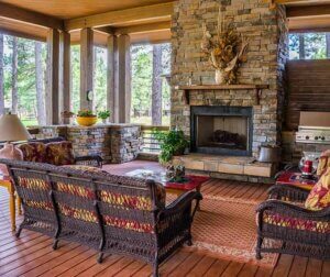 A four-season room with a large stone fireplace and comfortable seating, coffee table and lighting.