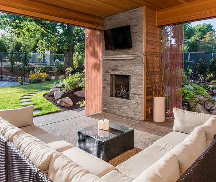 A covered outdoor room with a stone fireplace and comfortable seating.