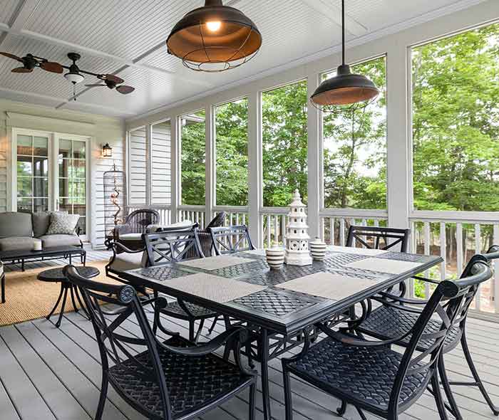 A screened-in porch has a dining table and chairs with elegant lighting and a ceiling fan.