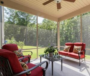 A screened porch with comfortable chairs, coffee table and ceiling fan.